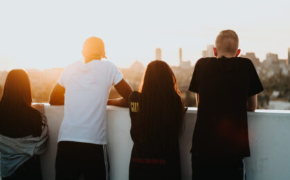 grupka nastolatków patrząca w stronę zachodzącego słońca